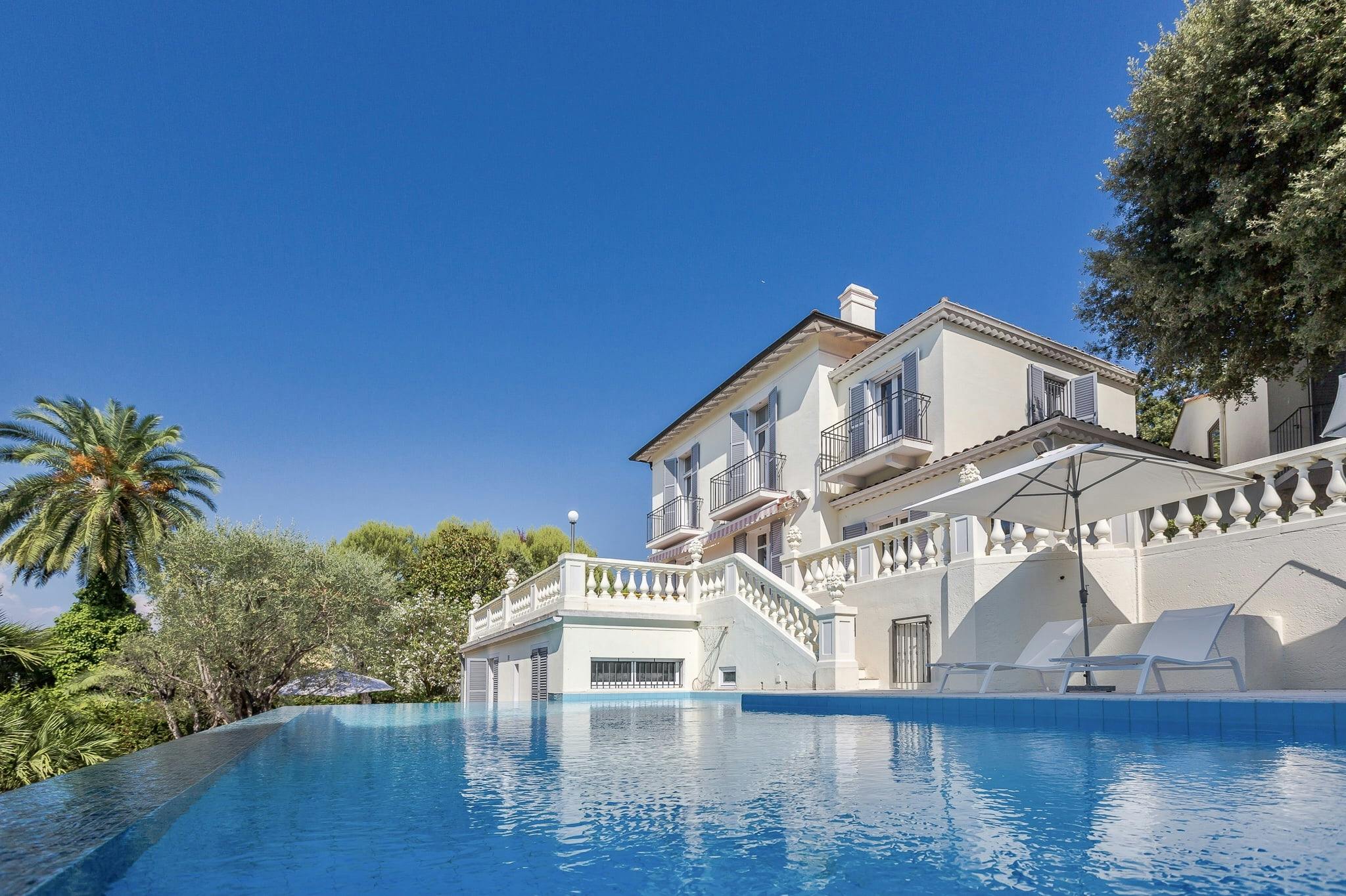 Villa Cosima et sa façade blanche, piscine en premier plan et ciel bleu