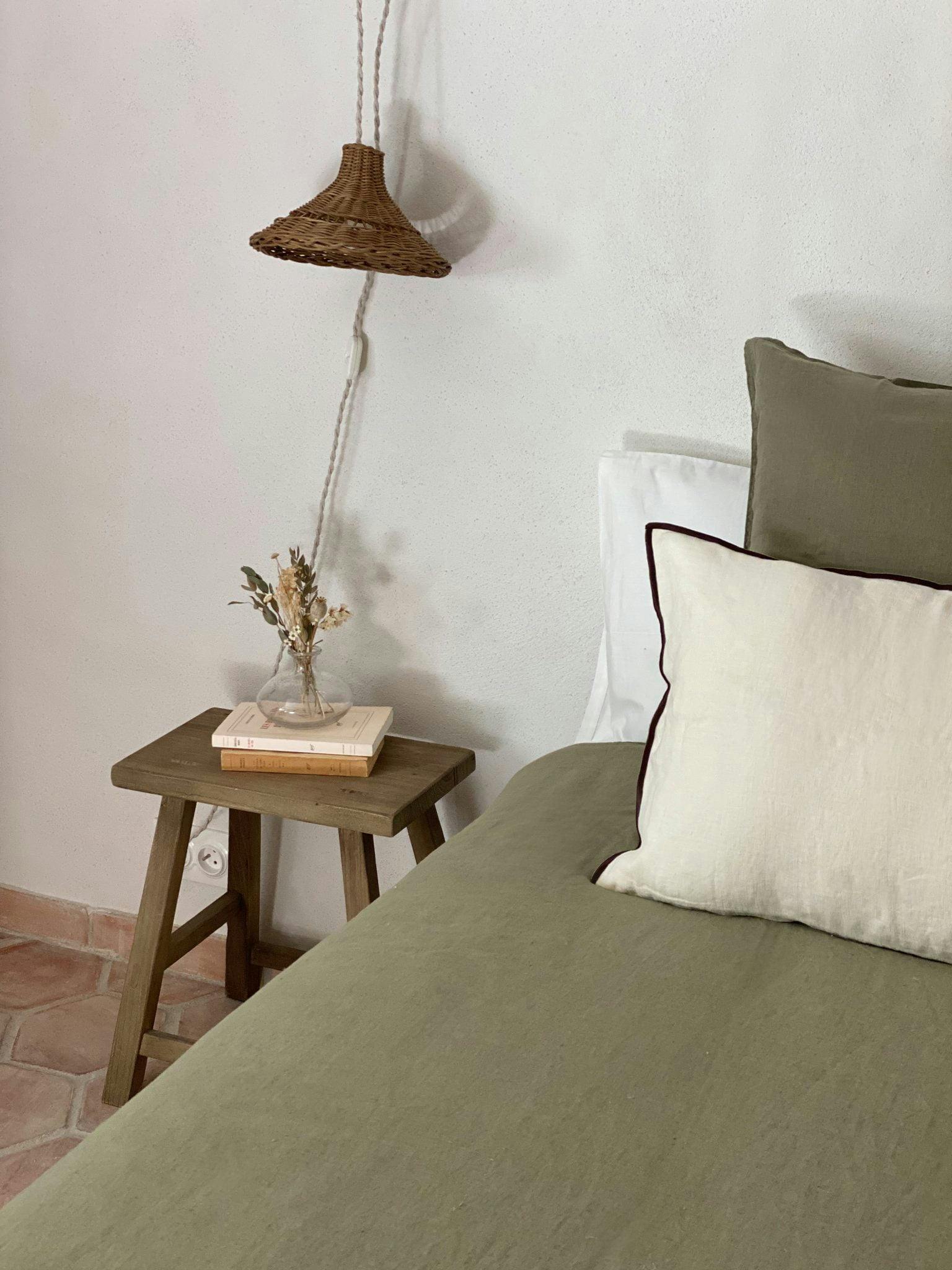 Détail de la table de nuit : tabouret en bois chiné à côté de la tête de lit et ses coussins