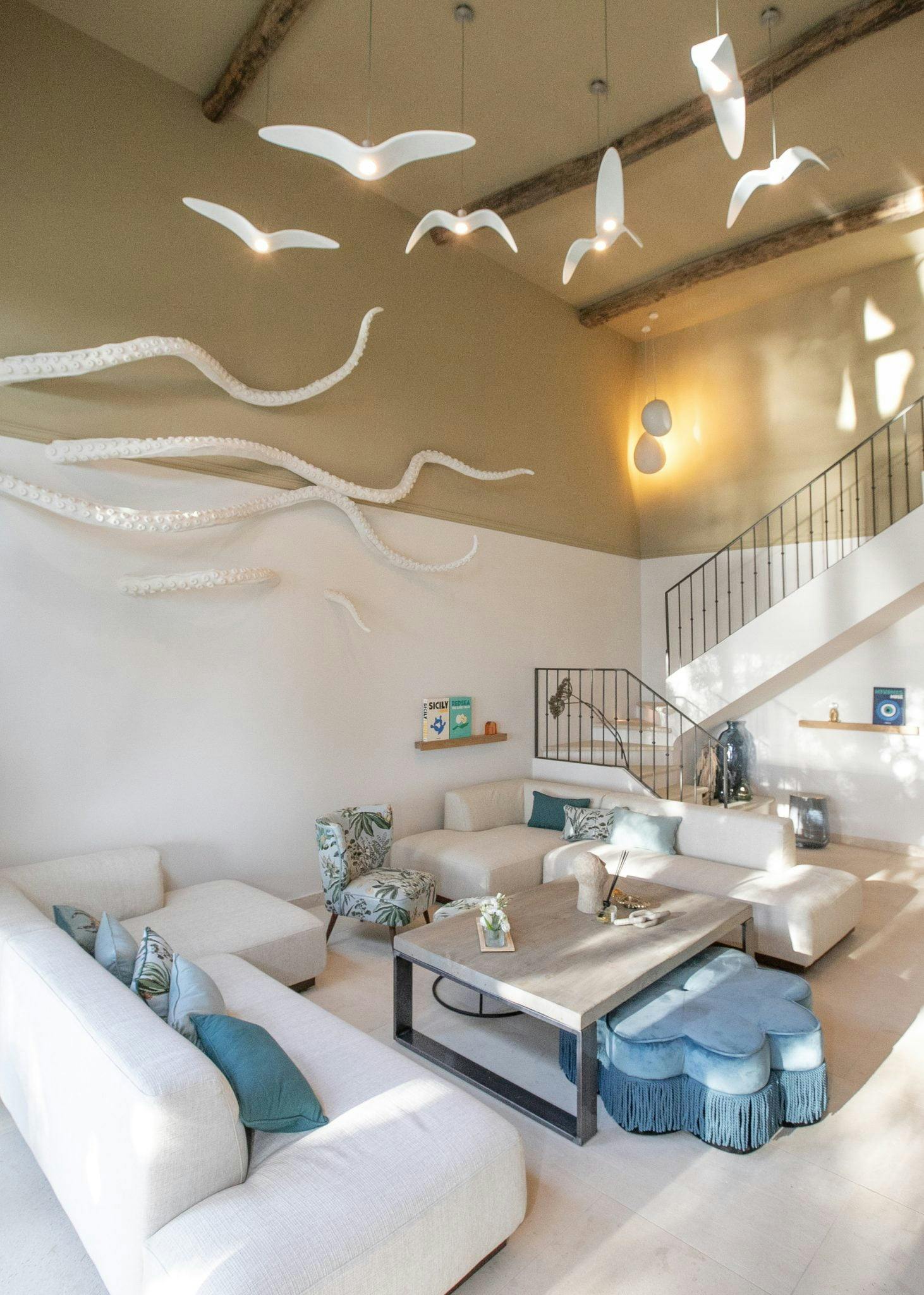 Salon décorée avec une sculpture d'octopus au mur, grand hauteur sous plafond, canapés blancs et oiseaux suspendus