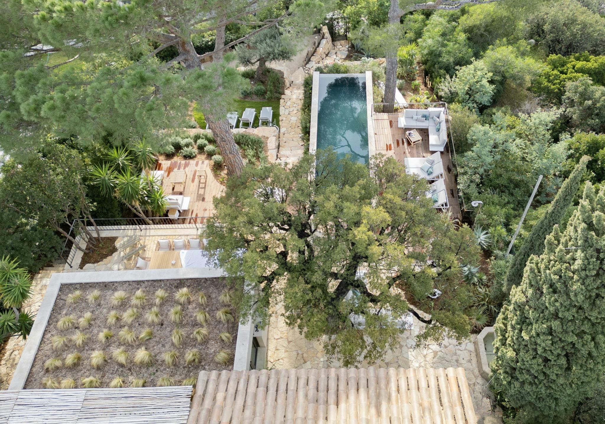Vue aérienne sur la maison, son toit, sa végétation et sa piscine devant la mer