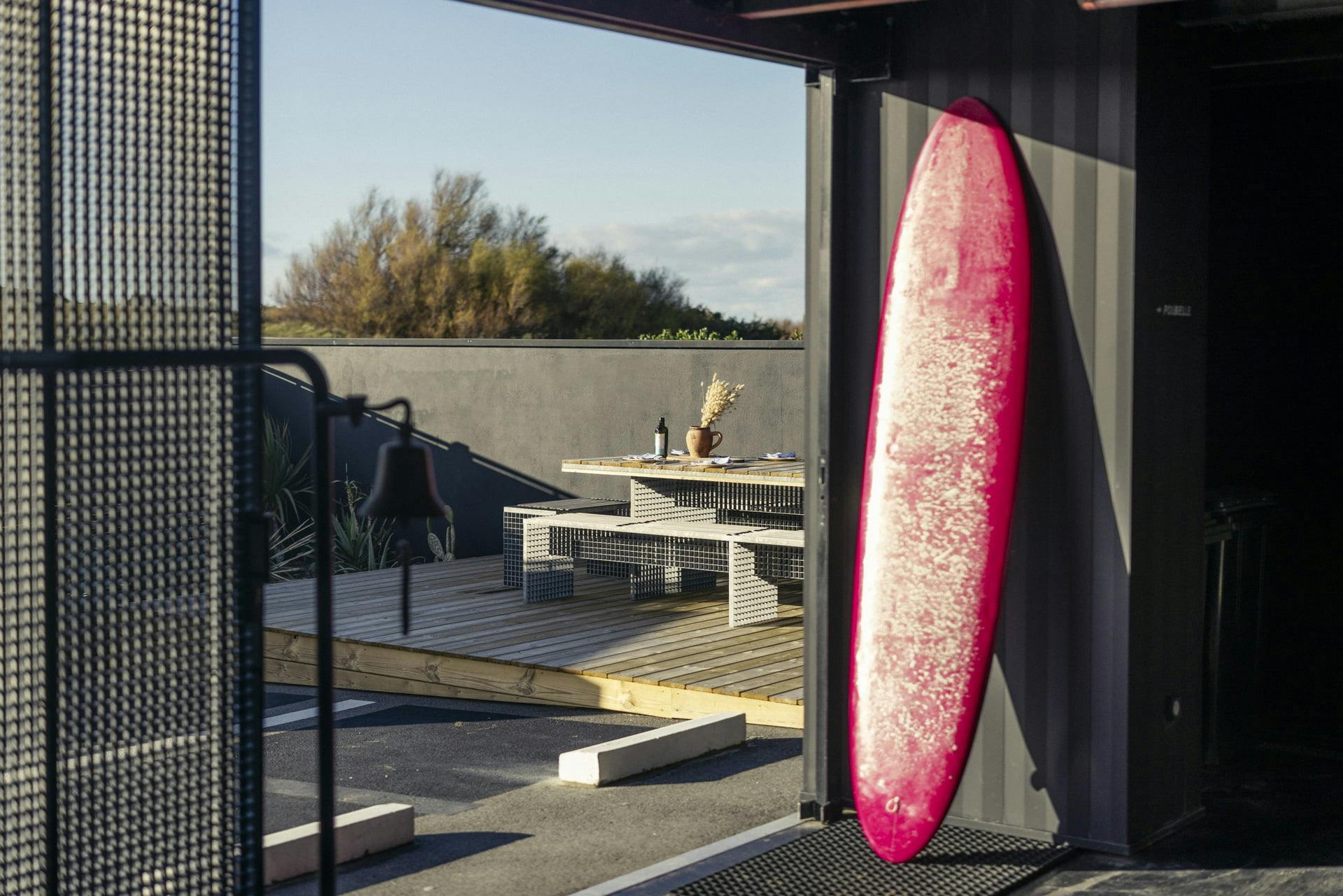 Planche de surf rouge adossée au mur donnant sur la large terrasse extérieure