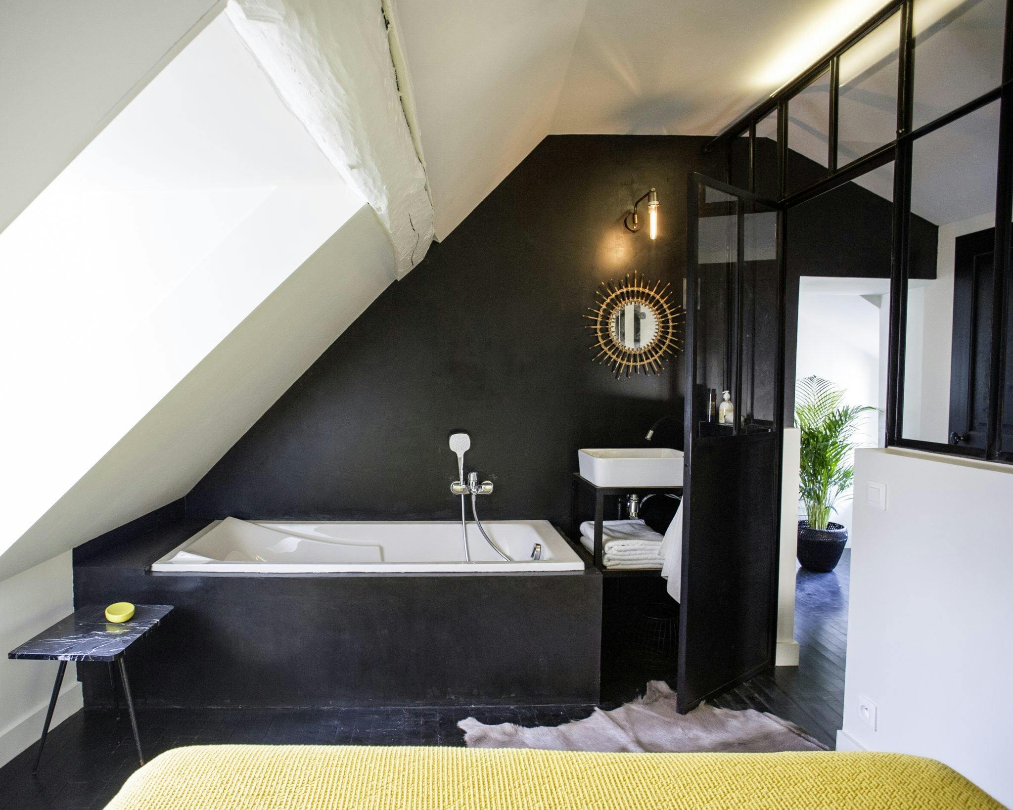 Détail de la salle de bain aux murs noirs, baignoire, baie vitrée et miroir doré.