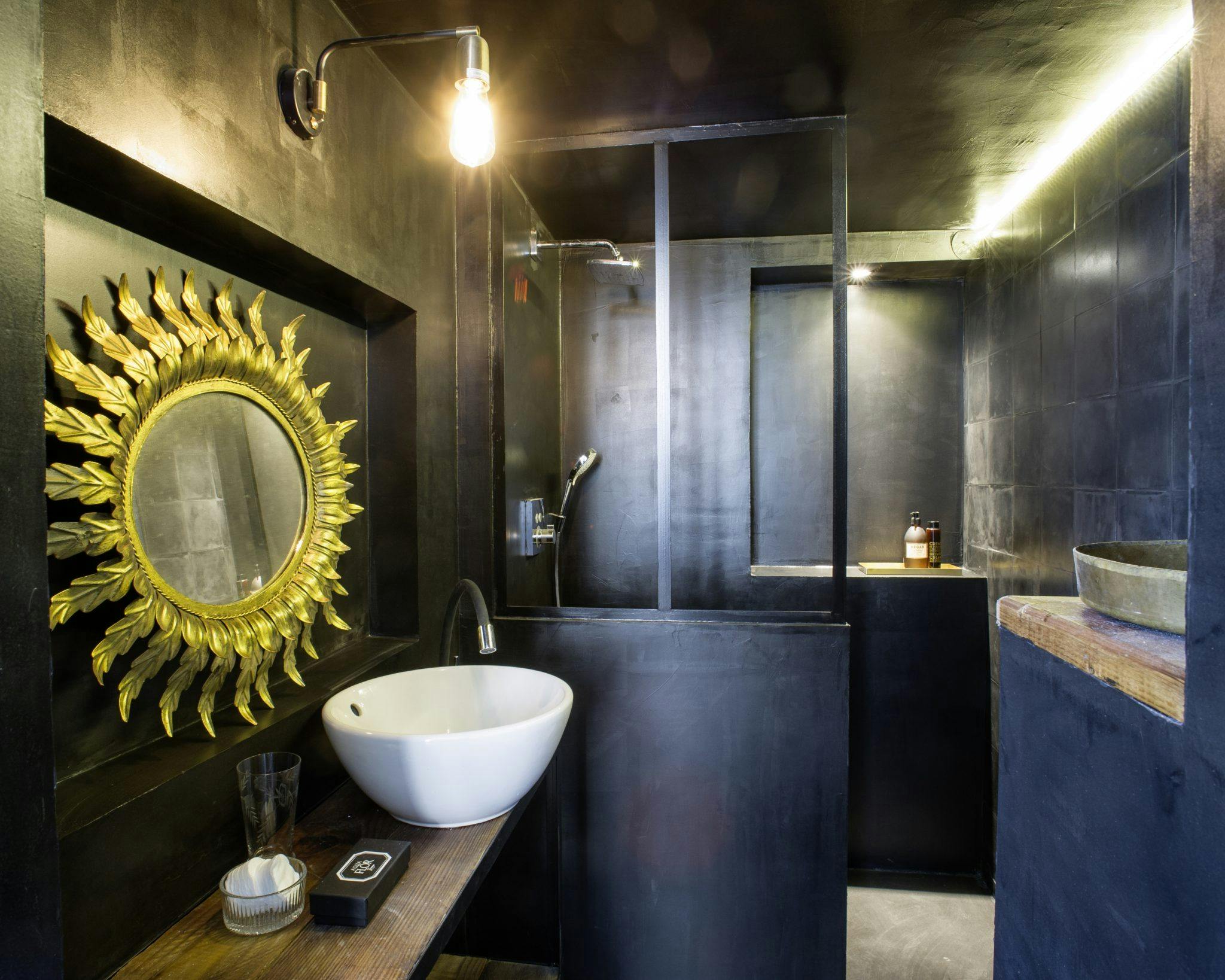 Détail de la salle de bain aux murs noirs, baie vitrée et miroir doré.
