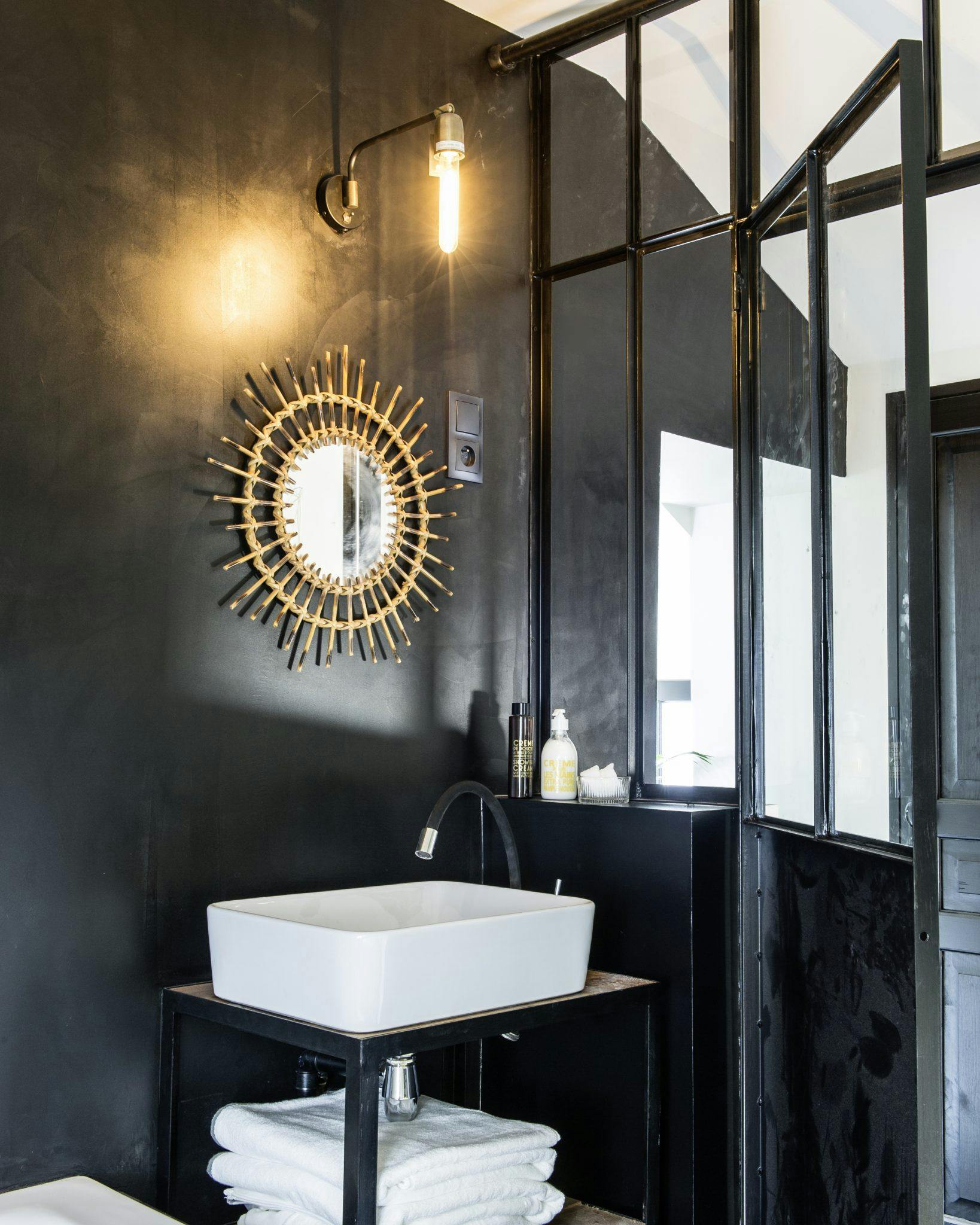 Détail de la salle de bain aux murs noirs, baie vitrée et miroir doré.