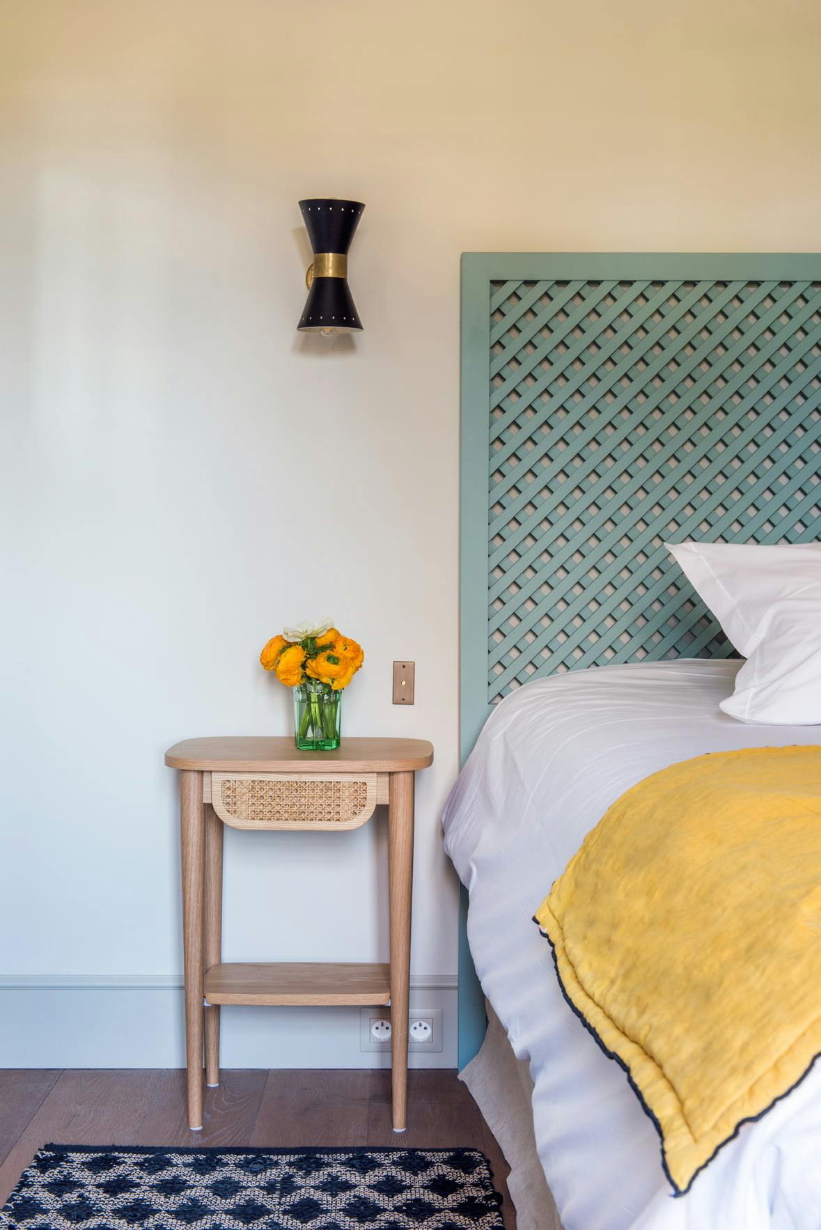 Détail de l'une des chambres du Mas le Gaudre : table de nuit en bois, tête de lit vert et dessus de lit jaune