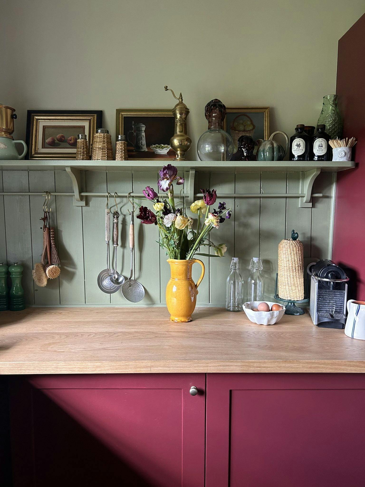 The kitchen of La Roquerie: red furniture and wooden countertop, bouquet of flowers