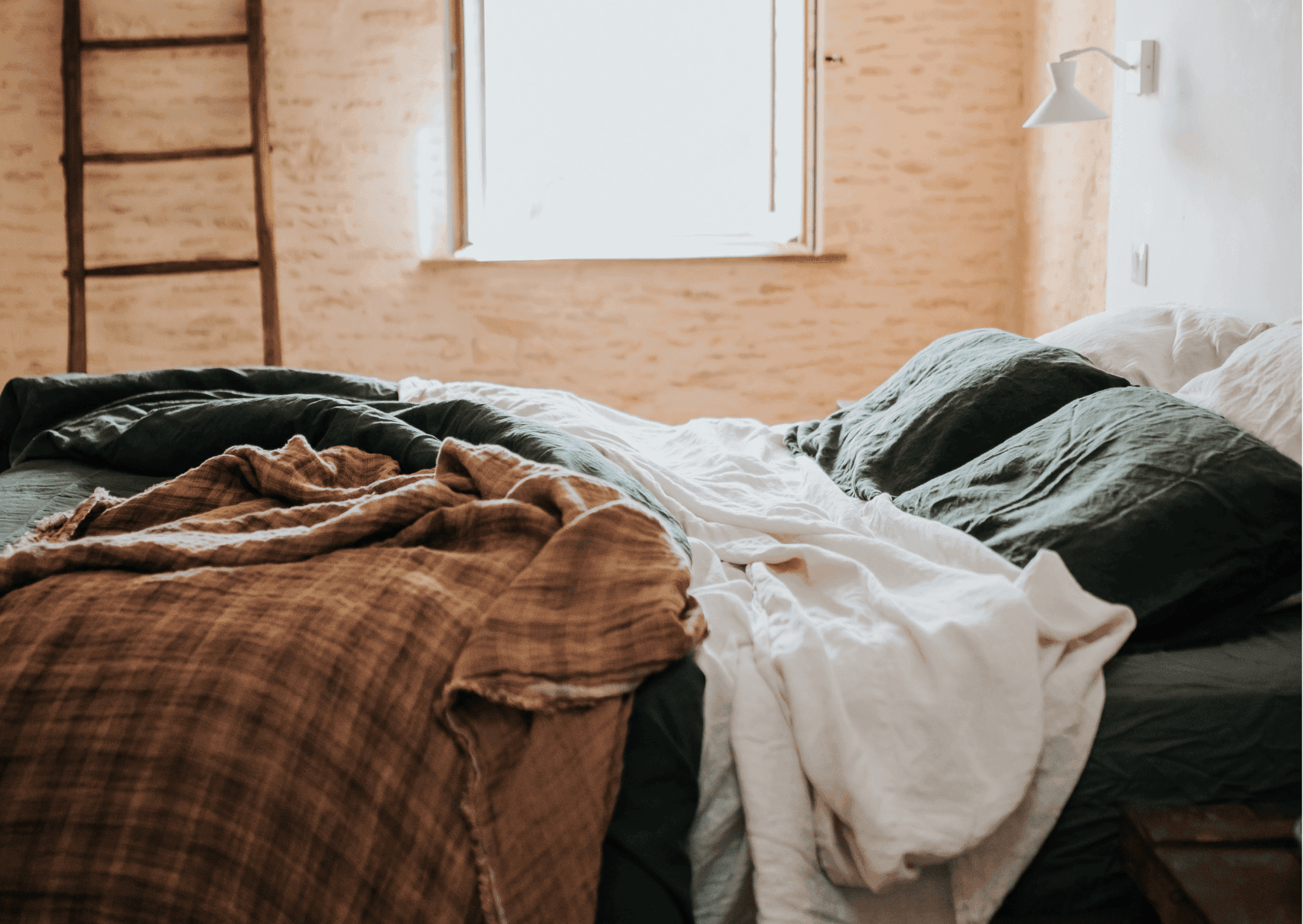 Draps défaits dans le lit de la chambre, échelle, mur en pierre