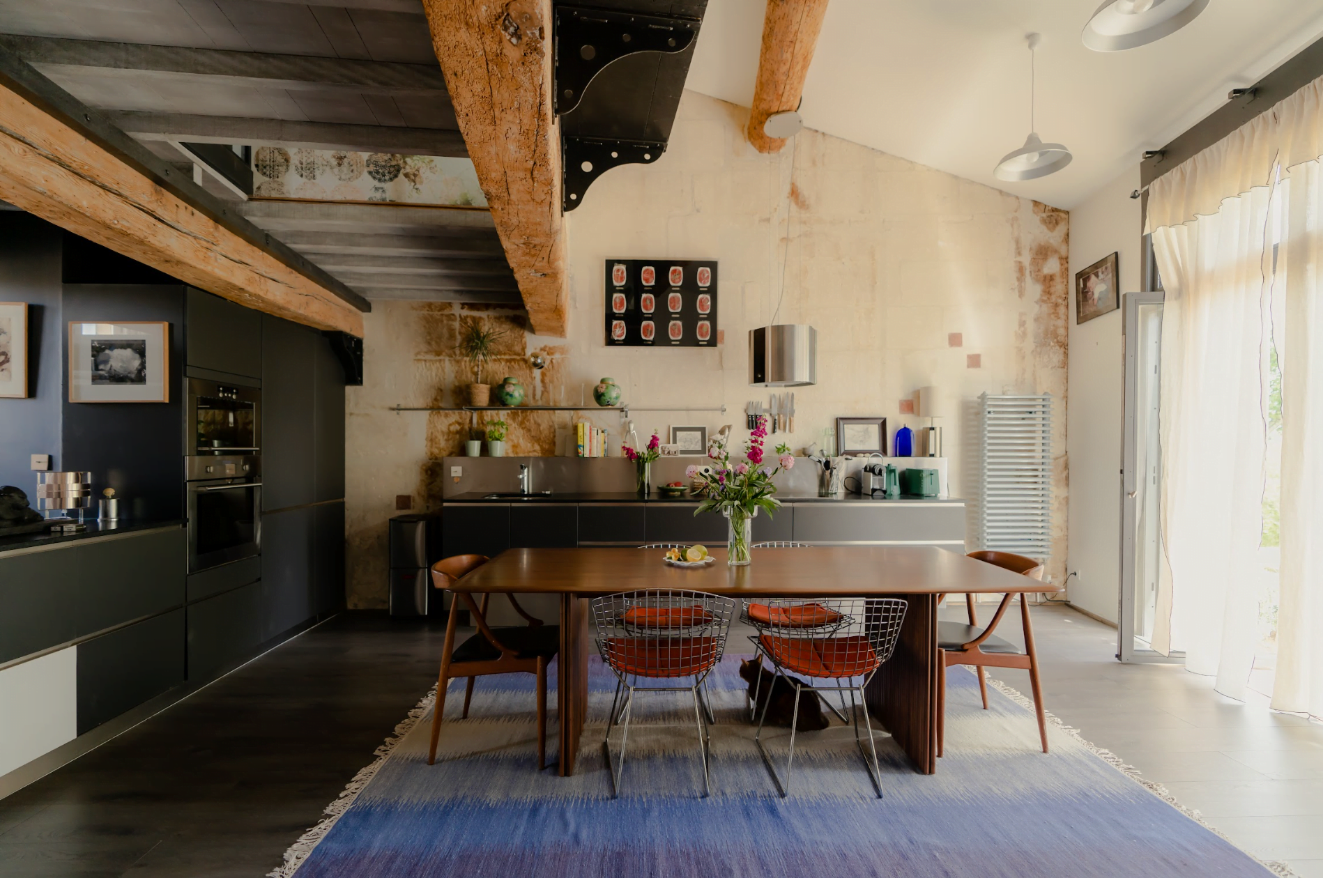 La salle à manger-cuisine : grande table en bois, poutres, tapis