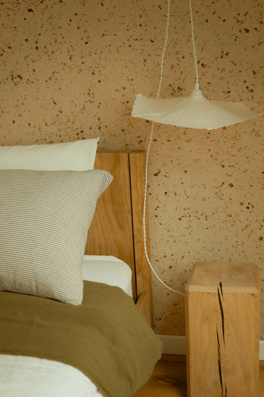 Détail d'une chambre : mur terrazzo, lit, suspension et table de nuit