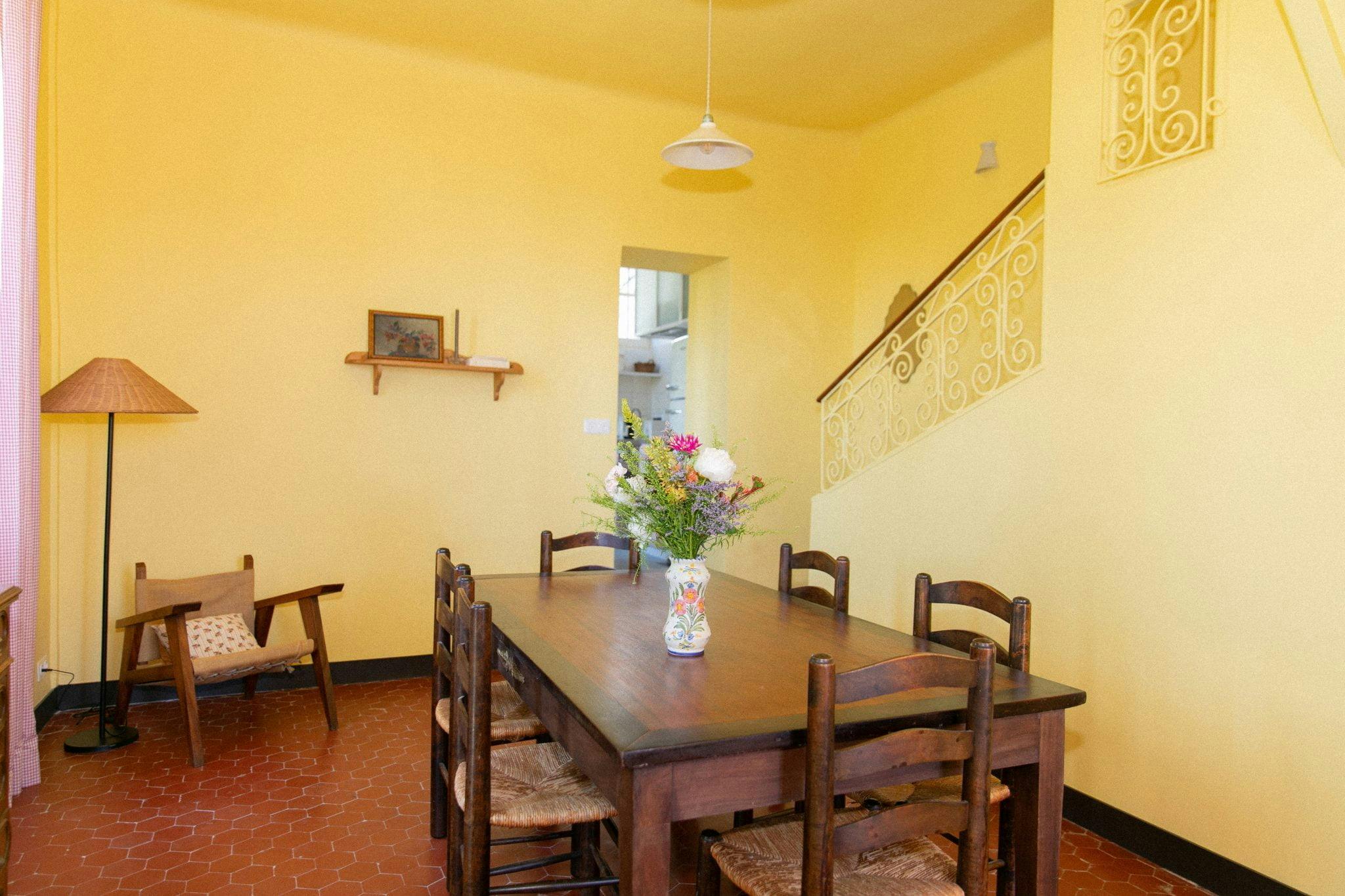 The dining room: wooden table and chairs, yellow walls, bouquet of flowers