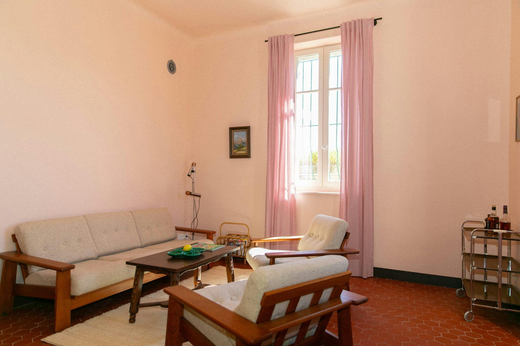 The living room of the villa: wooden armchairs, sofa, terracotta tiles, gingham curtains