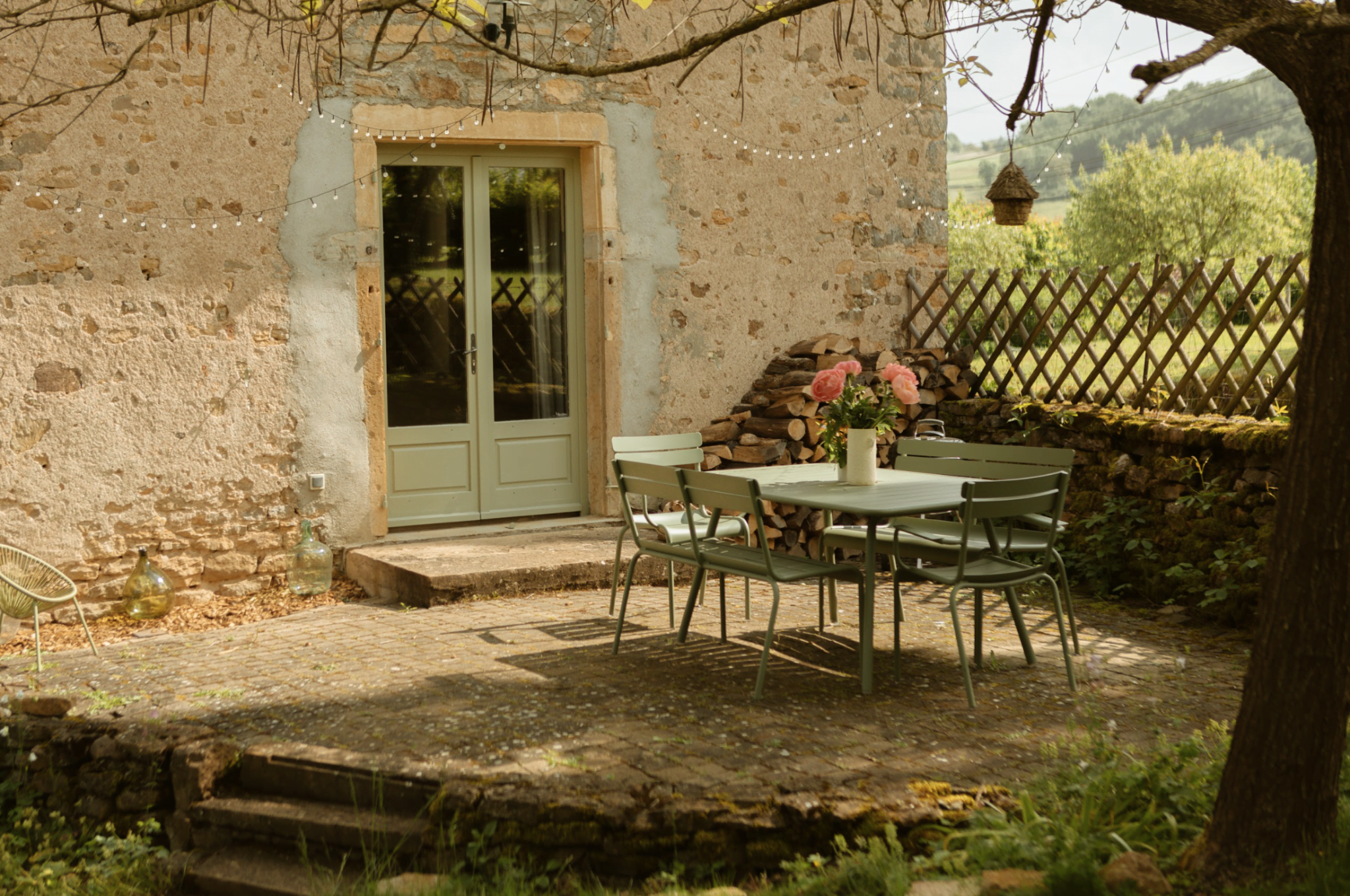 Table and garden chairs on the terrace, facade of a stone house.