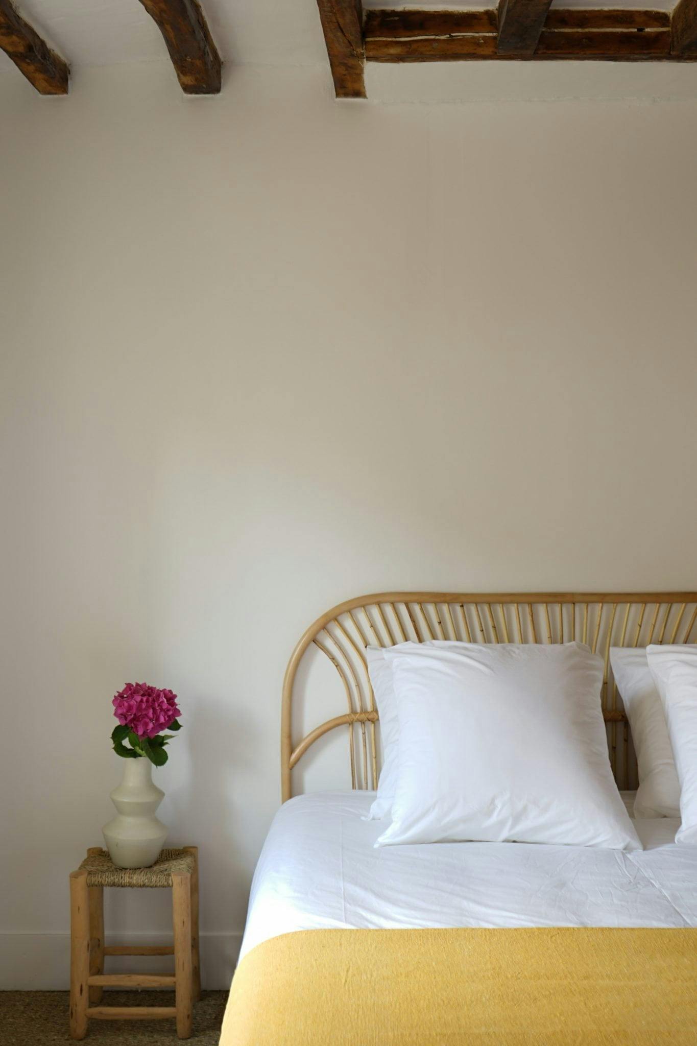 Detail of a bed in a bedroom, bedside table with a flower in a vase.