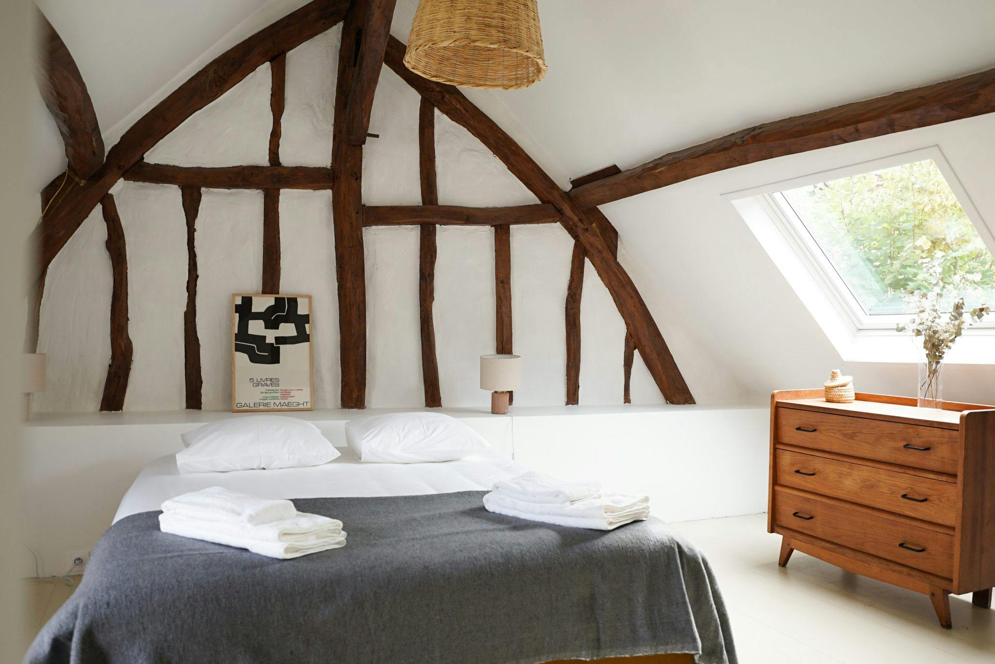 Bedroom with double bed, white and grey sheets, beams on the wall.