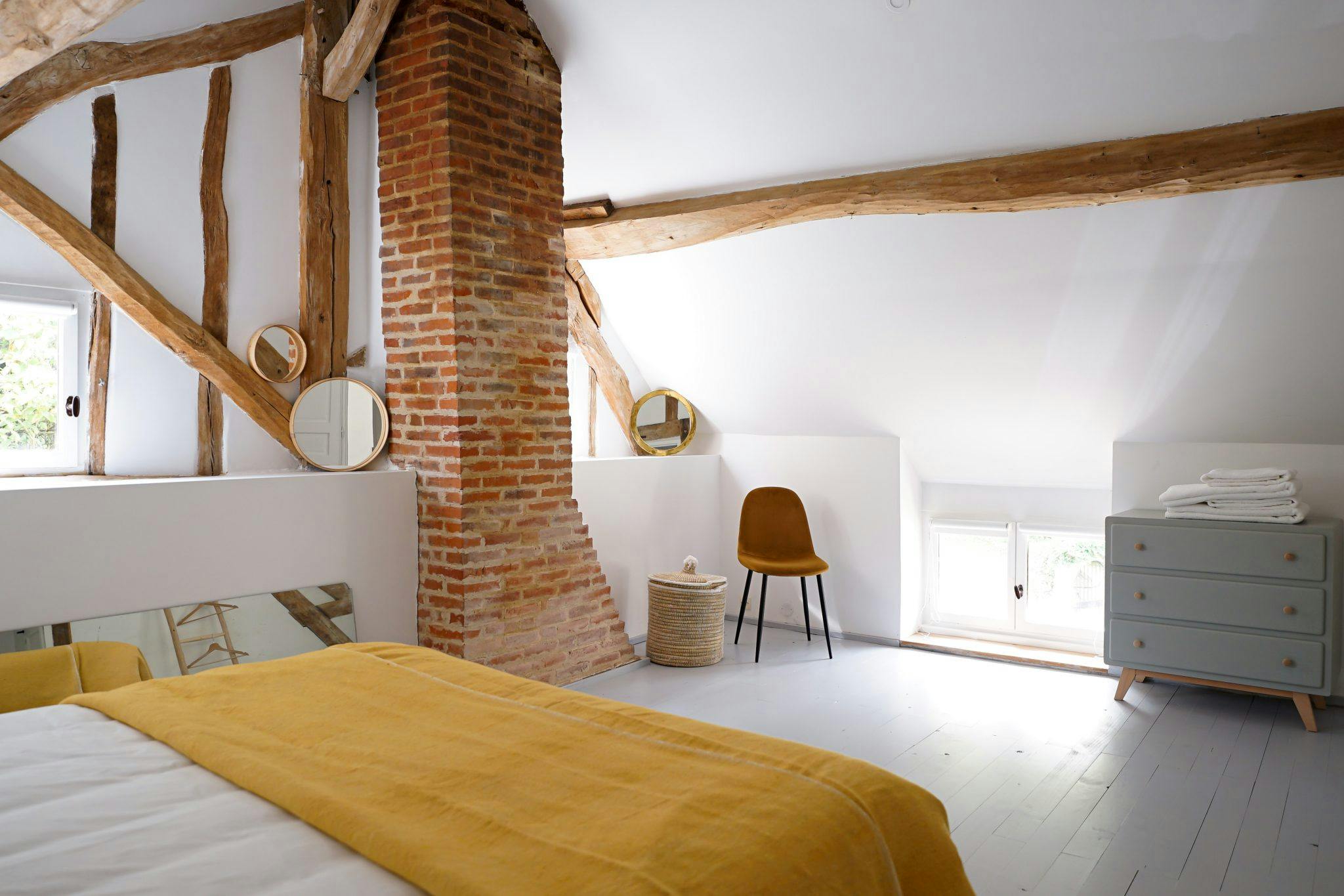 Bed with yellow sheets, brick fireplace, white hardwood floor.