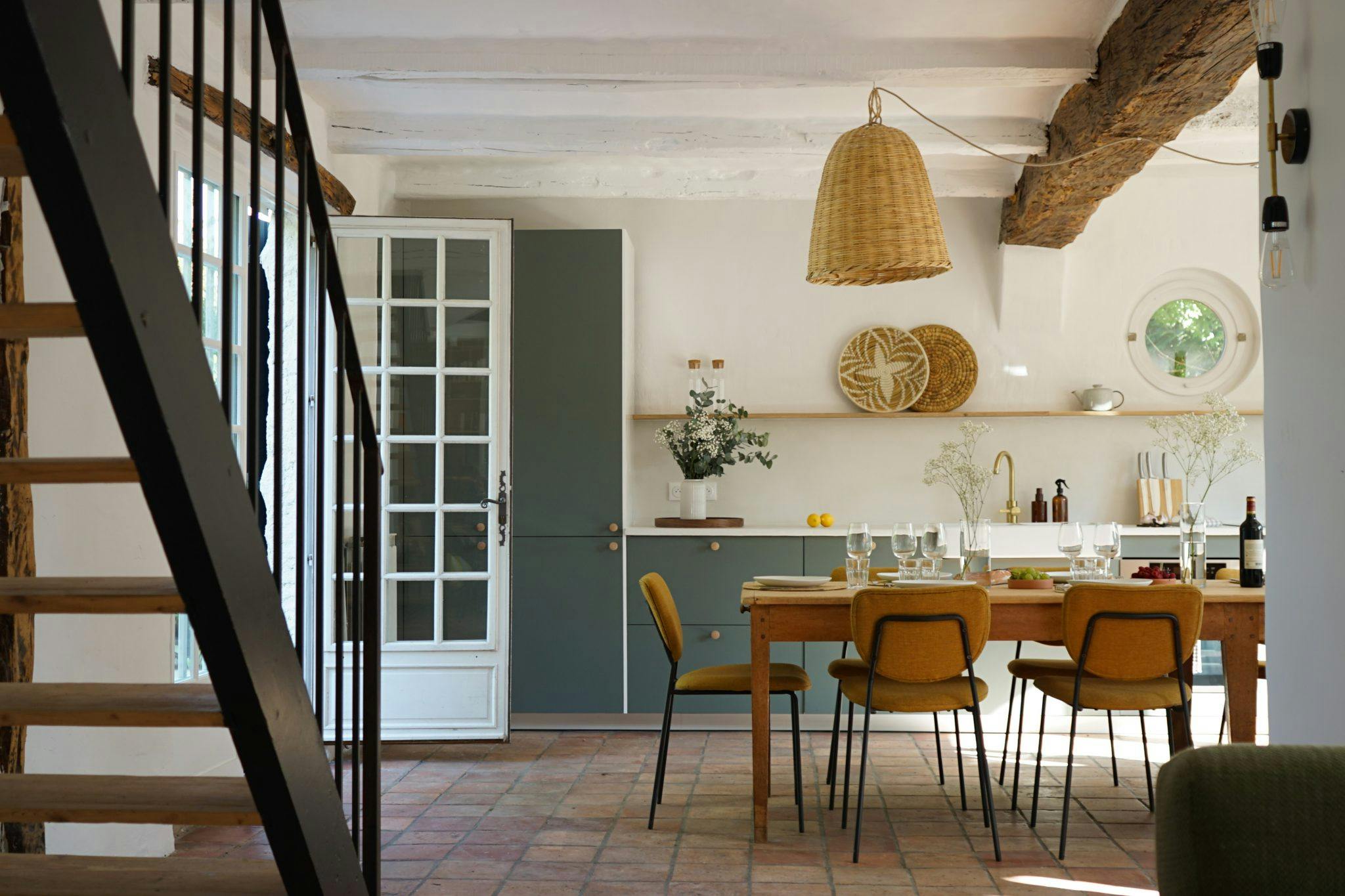 Cuisine salle à manger : escalier en bois, grande table dressée, chaises, suspensions