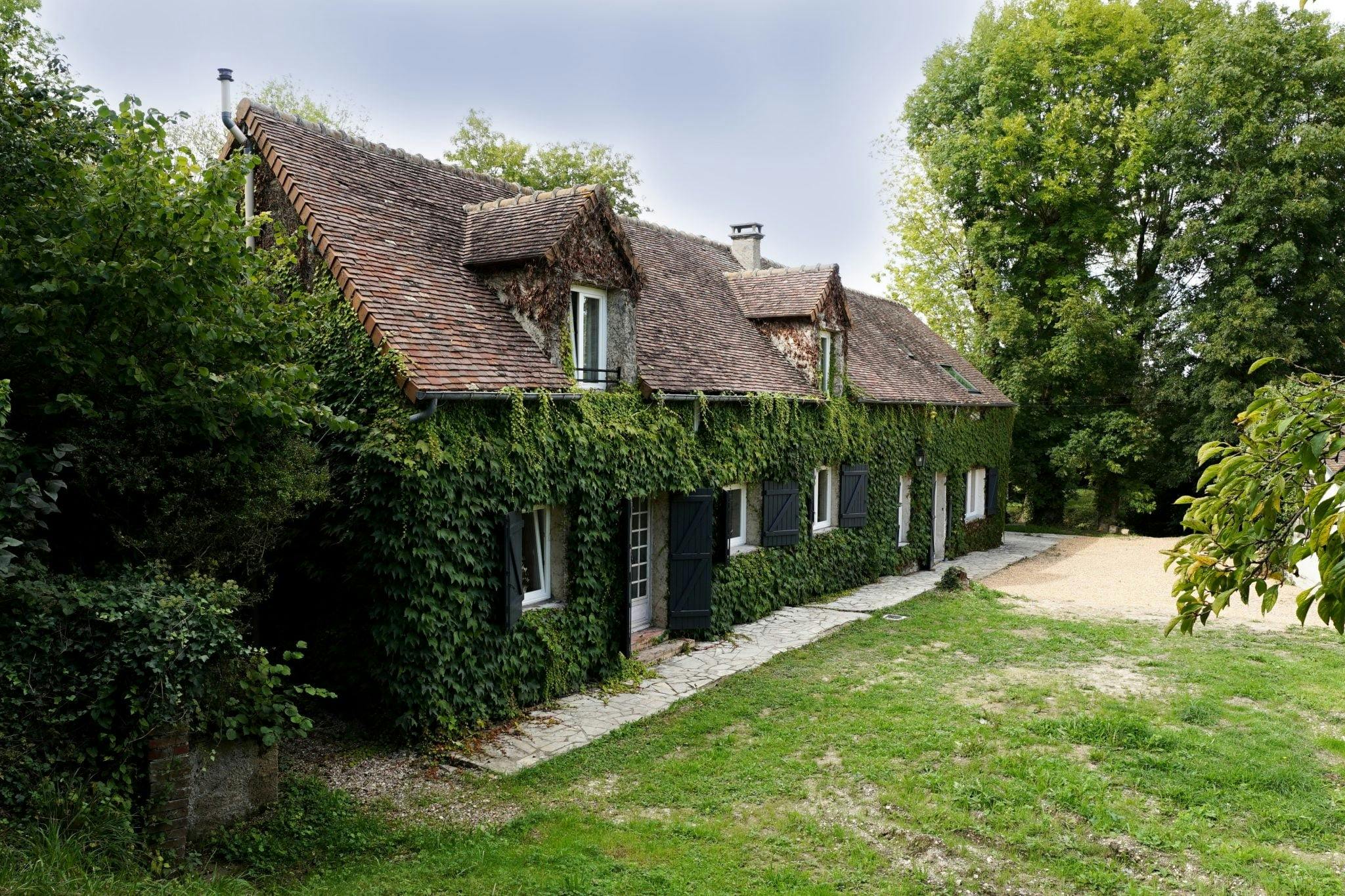 The facade of the house covered in ivy-covered stone, with a lawn in the foreground.