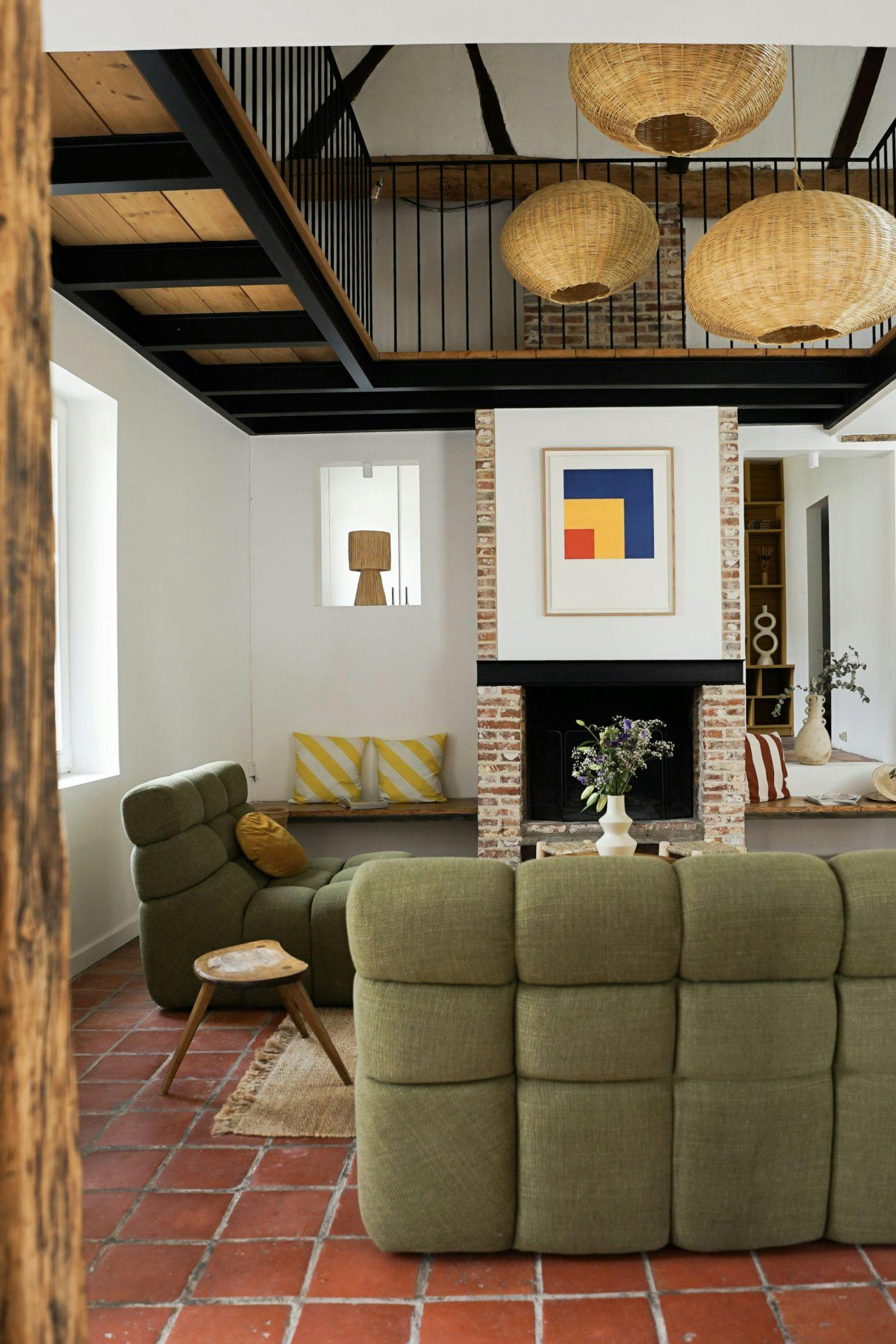 Green sofa, pendant lights, painting above the fireplace, terracotta tiles on the floor.