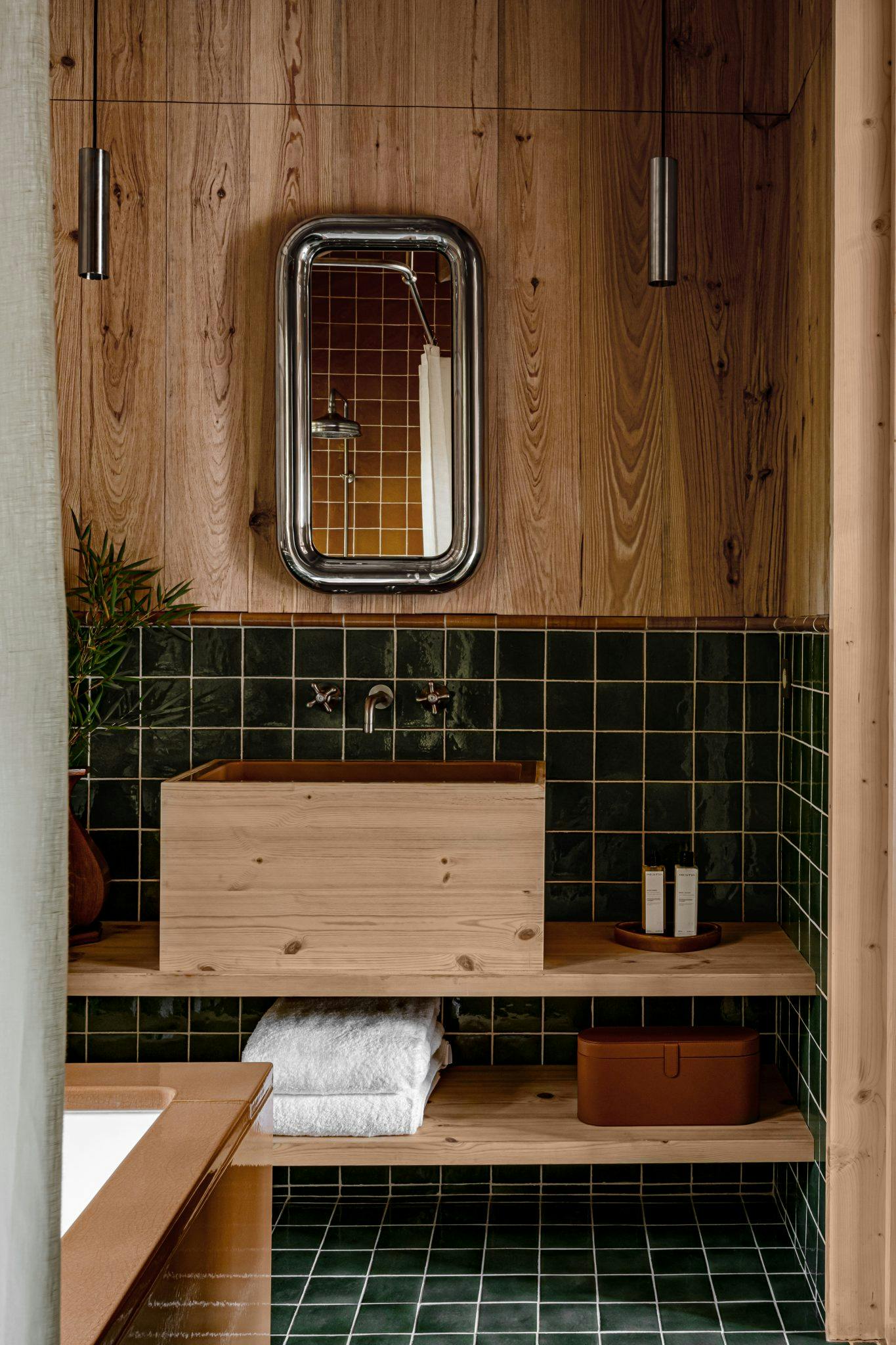 Détail de la salle de bain: carreaux verts, murs en bois, lavabo, miroir