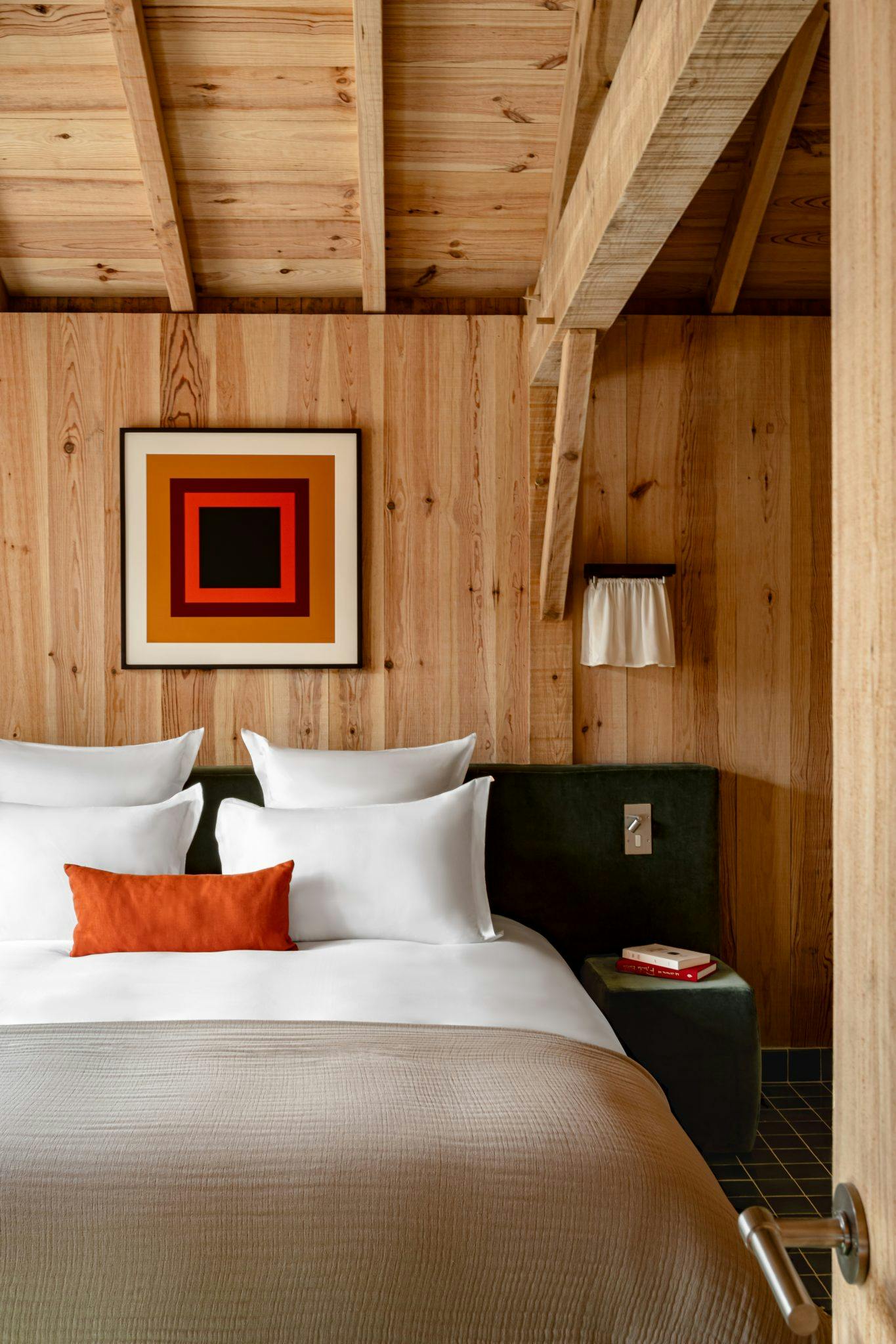 Nightstand, bed with white sheets, small lamp, and painting on the wooden wall