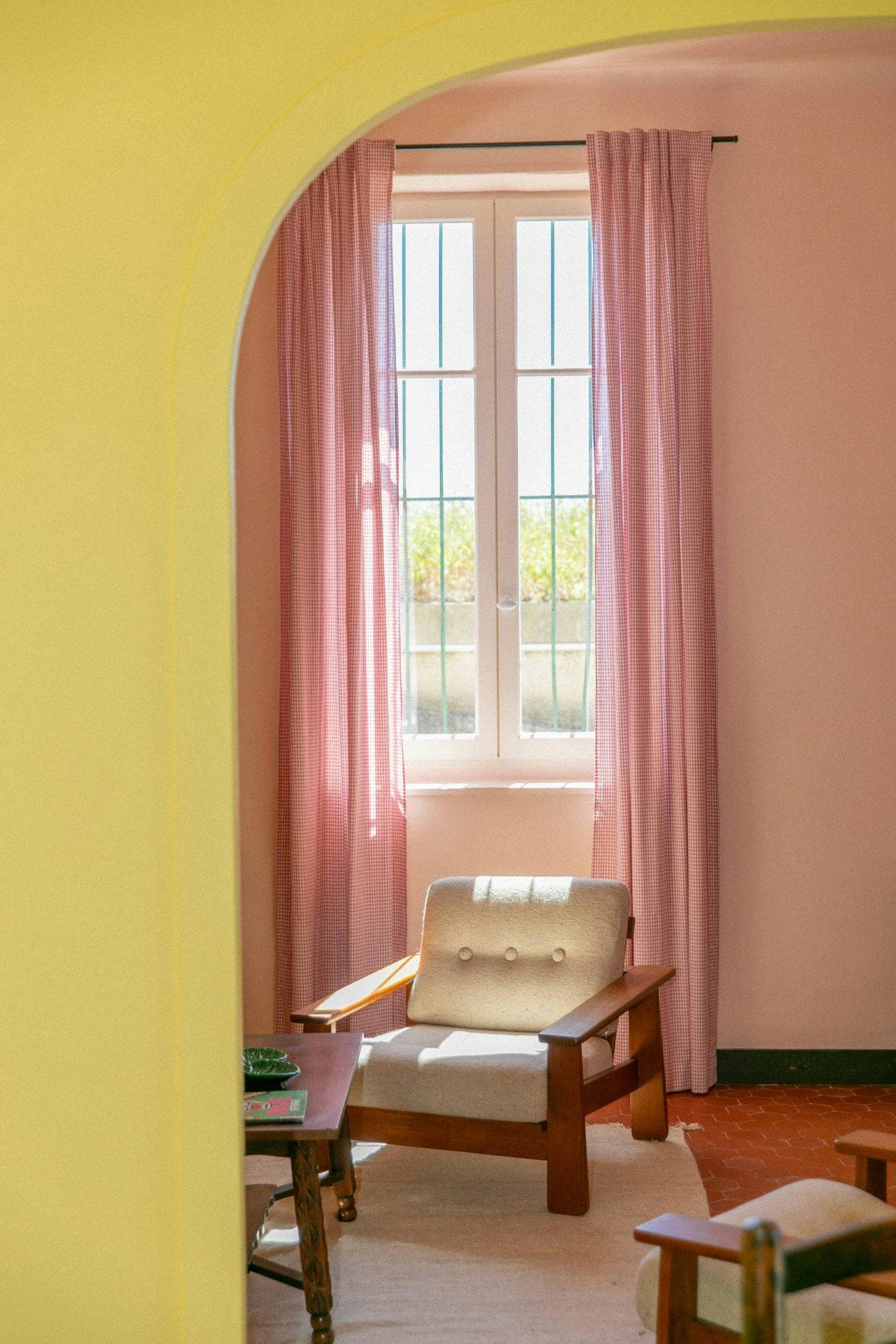 Fauteuil dans le salon, mur jaune, rideaux roses