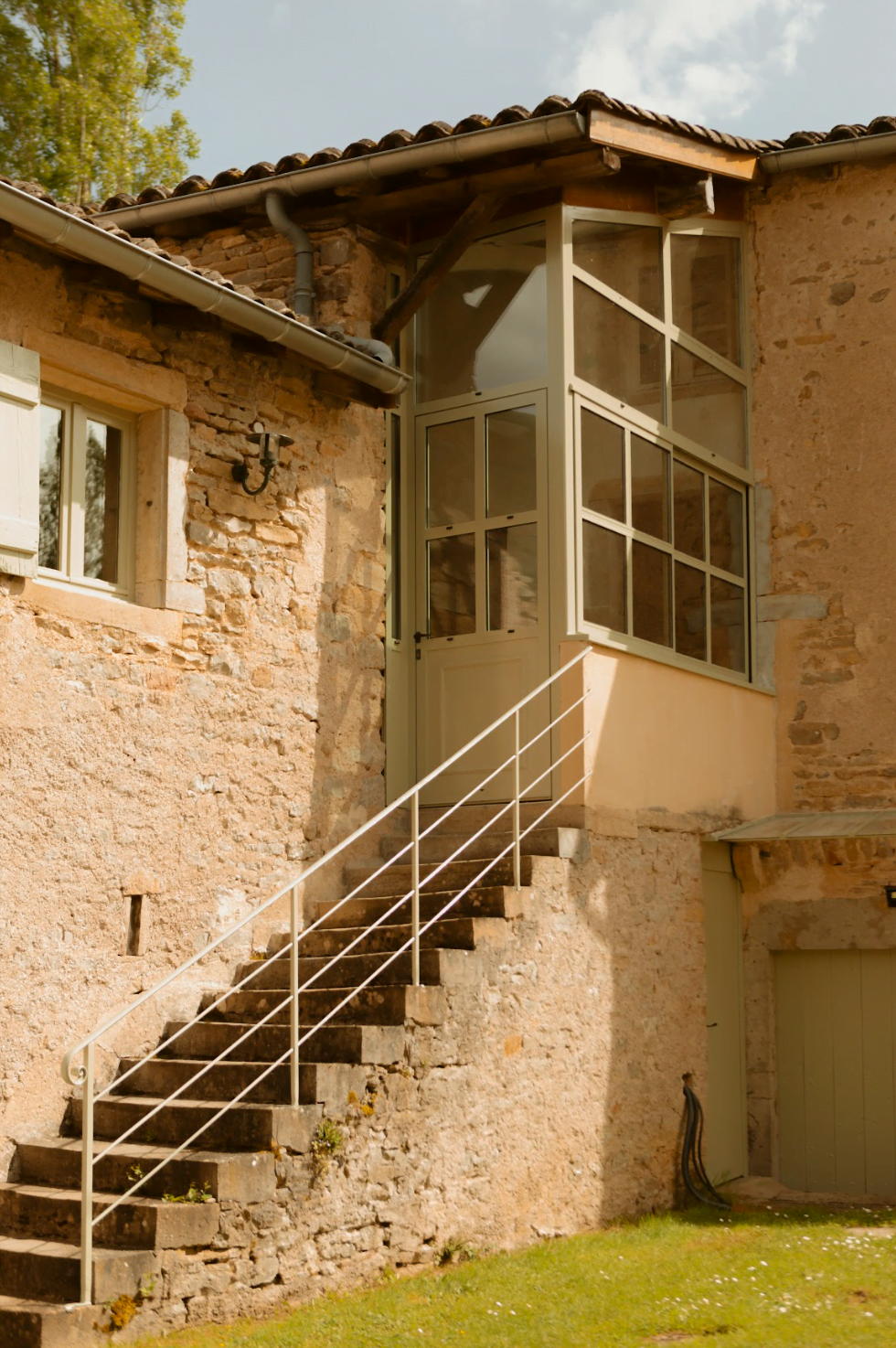 Escalier en pierre menant à une petite véranda, mur en pierre, pelouse au premier plan