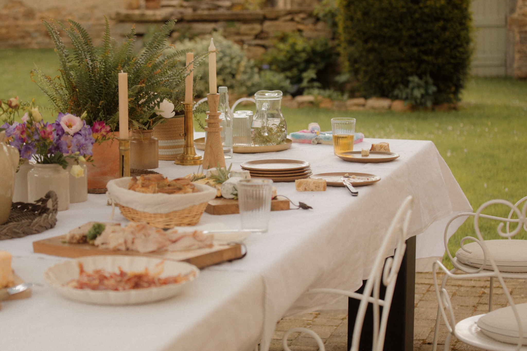 Table avec nappe blanche dressée dans le jardin : bougeoirs, plats, assiettes