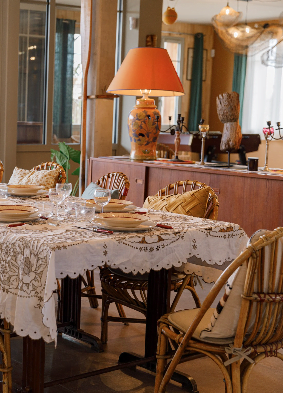 Table set with a tablecloth, wooden chairs, and an orange light fixture.