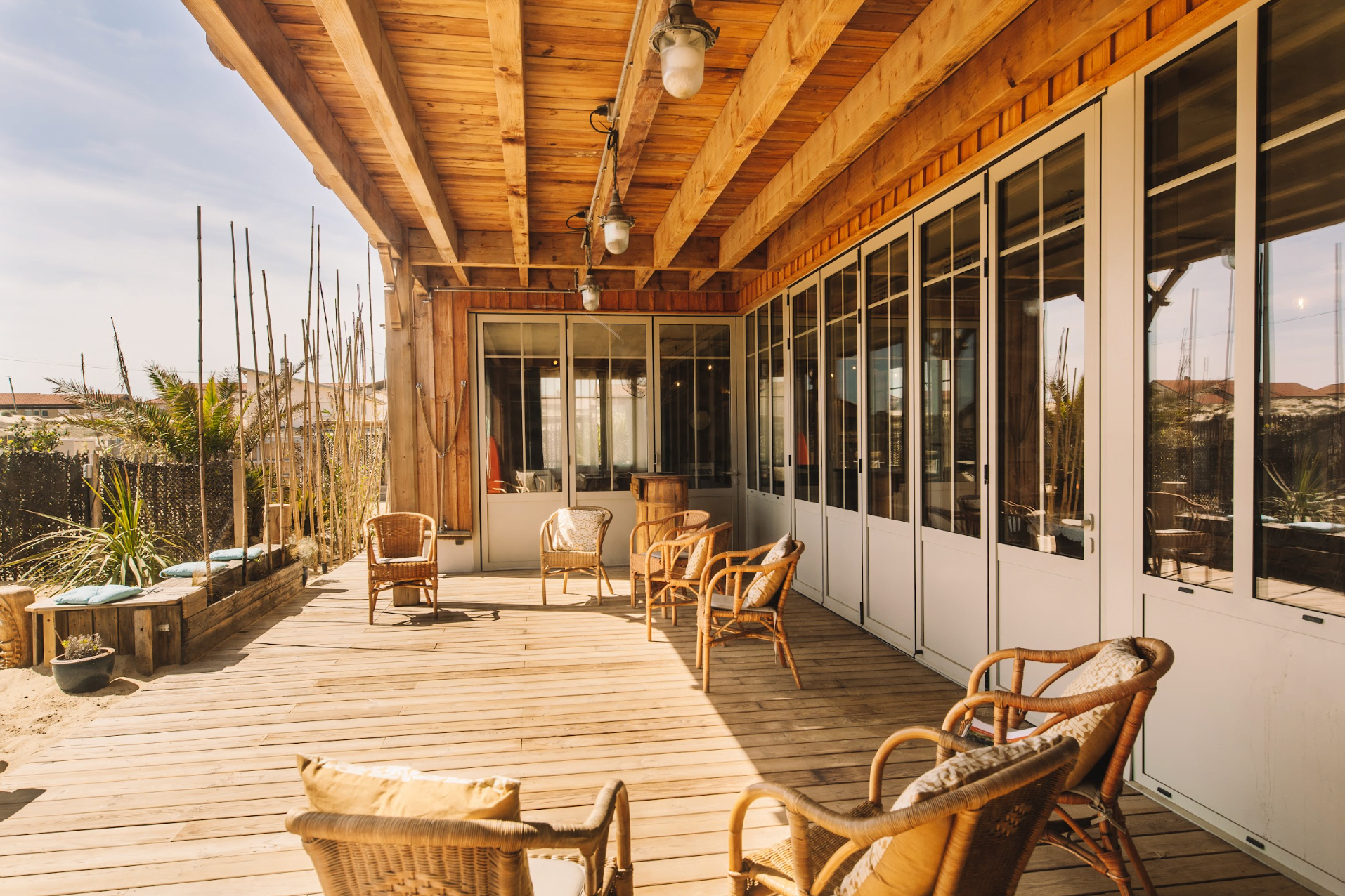 Wooden terrace, rattan chairs, floor-to-ceiling windows.