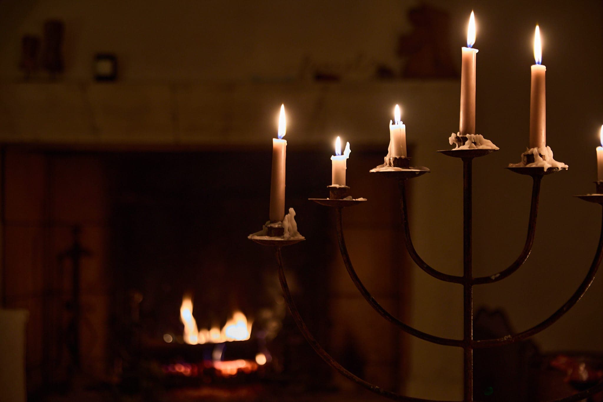 Au premier plan, un candélabre avec des bougies allumées et, à l'arrière-plan, une cheminée allumée. La scène est faiblement éclairée, créant une atmosphère chaleureuse et confortable.