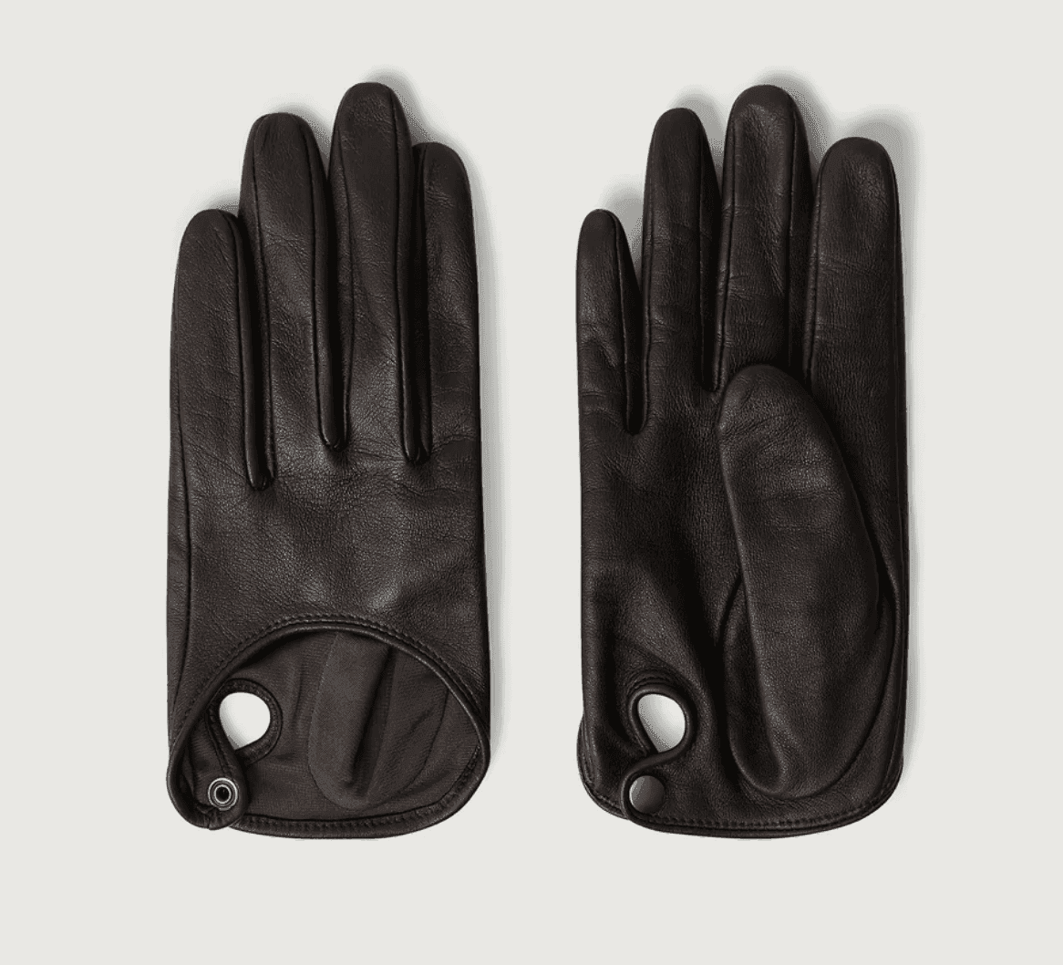 Une paire de gants en cuir noir est exposée. Le gant gauche est ouvert pour montrer la doublure intérieure marron, avec un petit œillet circulaire près du poignet. Le gant droit est fermé, montrant l'extérieur complet.