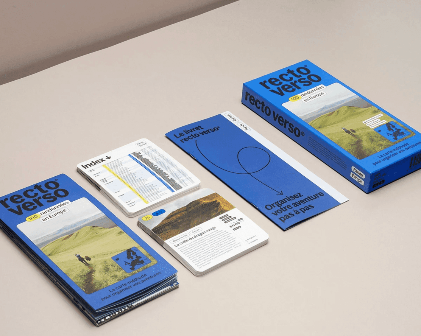 Un ensemble de guides de voyage intitulé « recto verso » pour 150 micro-aventures en Europe est présenté sur une surface beige. L'ensemble comprend un coffret, des livrets et une brochure avec des images panoramiques et des cartes.