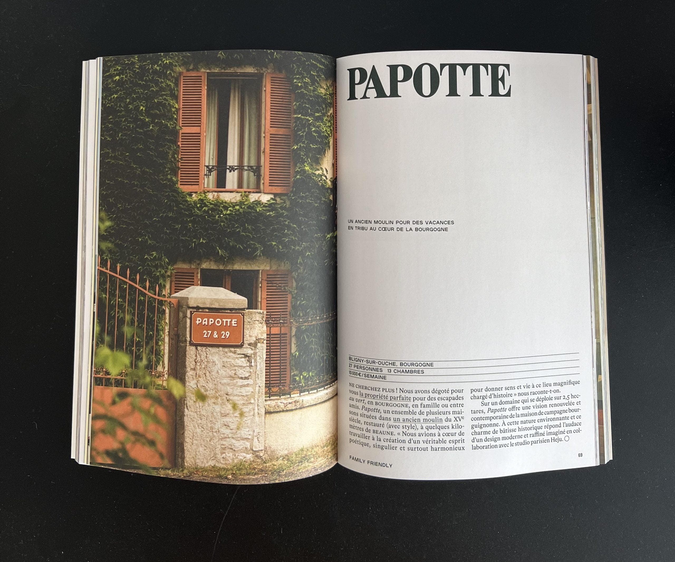 An open magazine shows a photo of a house with red shutters and greenery on the left page, and the title “PAPOTTE” with French text on the right page. A stone mailbox labeled "PAPOTTE 27 R. 19" is in front of the house.